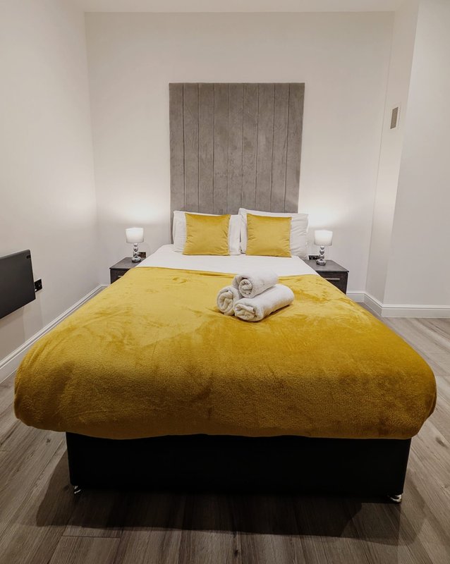 Modern bedroom with double bed, yellow bedding, gray headboard and white bedside lamps