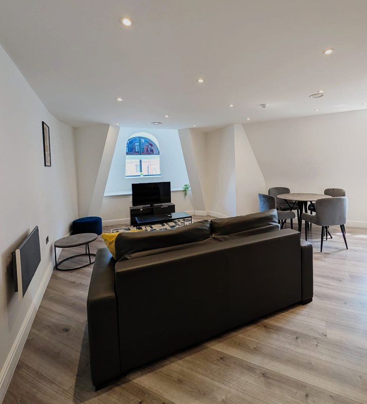 Modern open-plan living area with black sofa, TV, dining table and angled ceiling with skylight