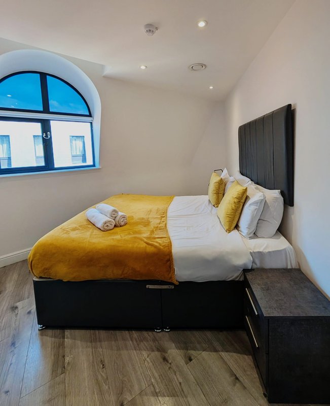 Modern bedroom with double bed, yellow bedding, black headboard and arched window