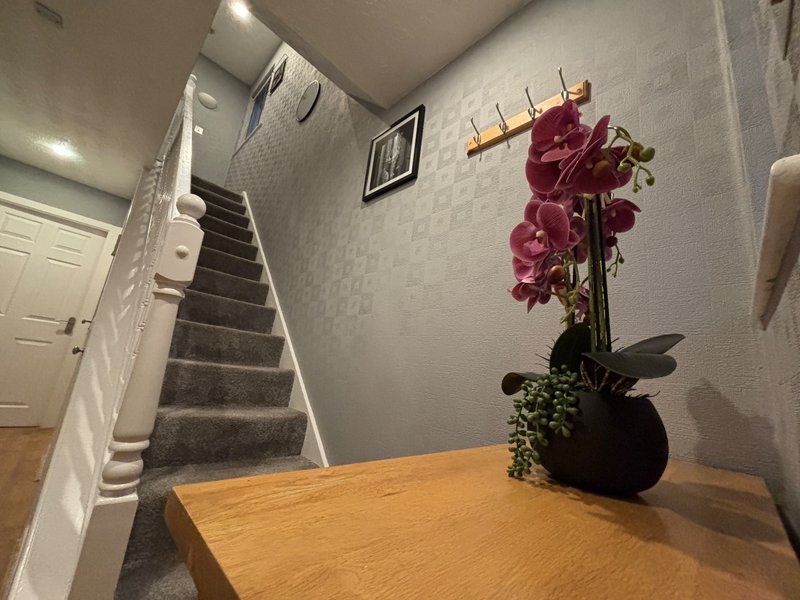 Hallway with wooden table, potted orchid plant, and staircase with white railings