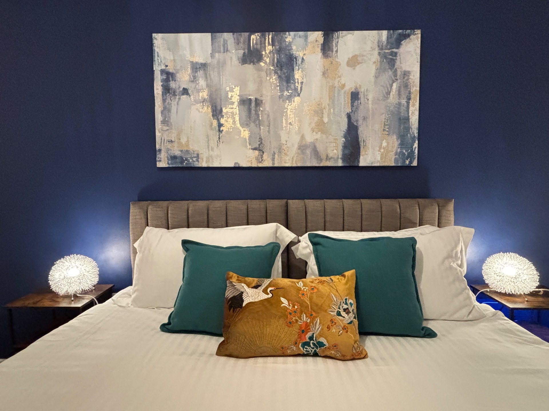 Modern bedroom with upholstered headboard, decorative pillows, bedside lamps and abstract wall art