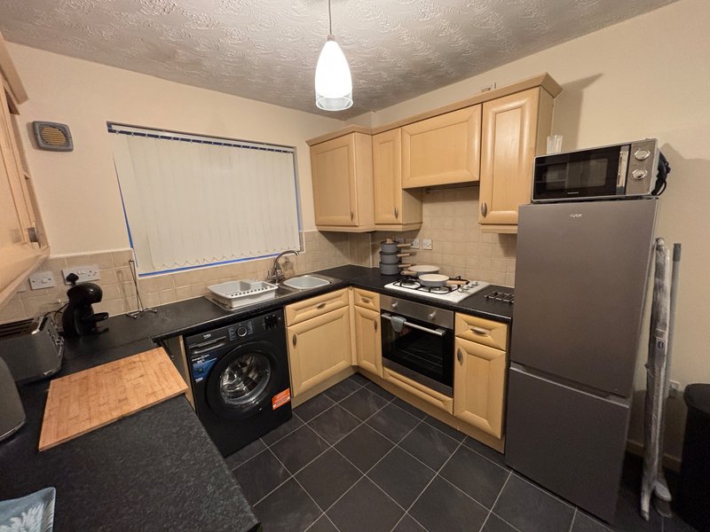 Kitchen with wooden cabinets, black countertops, stainless steel appliances and black tile floor
