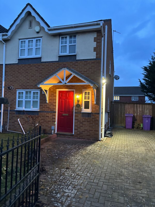 Two-story brick house with red door, lit porch, driveway and front garden at dusk