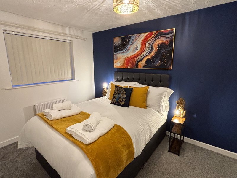 Modern bedroom with double bed, navy accent wall, gold bedding, framed artwork and bedside lighting