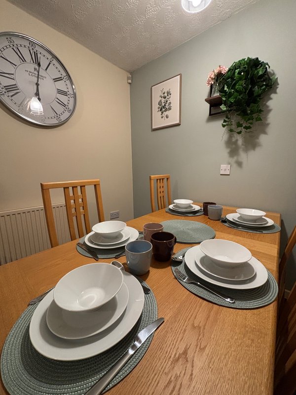 Dining room with wooden table set for four, wall clock, framed art, and hanging plant