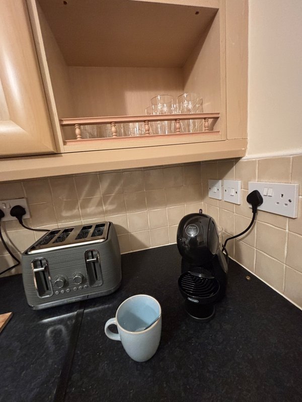 Kitchen countertop with toaster, coffee machine, mug, and open wall cupboard with glassware