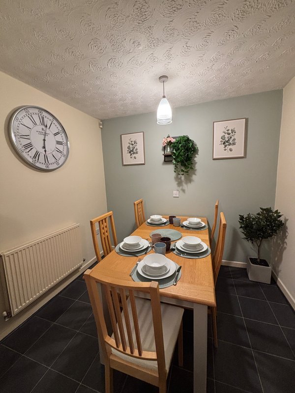 Dining room with wooden table, four chairs, place settings, wall clock and botanical prints