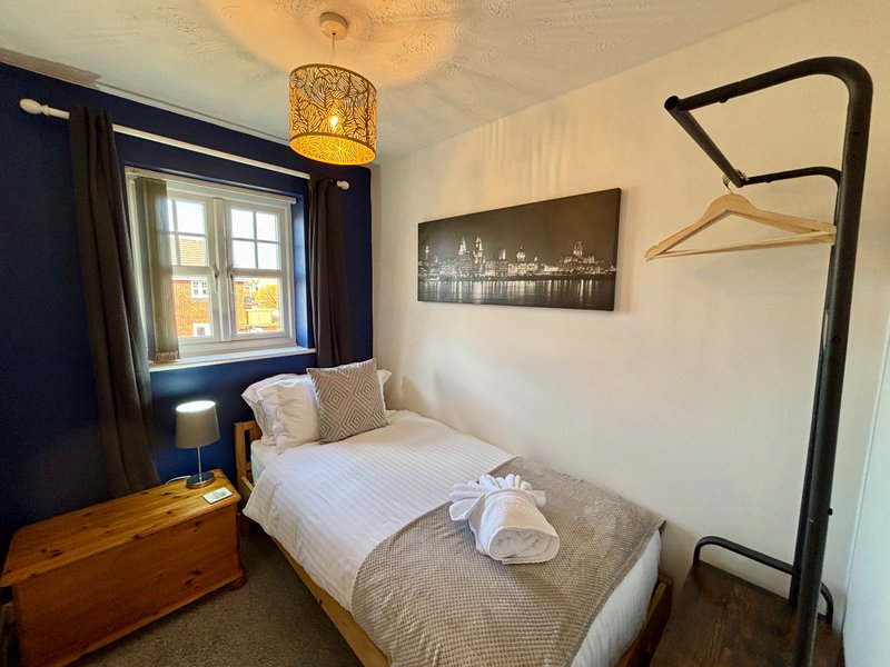 Compact bedroom with single bed, wooden desk, navy door, and pendant light fixture