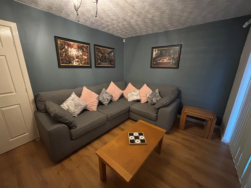 Living room with gray corner sofa, pink cushions, wooden coffee table, and framed wall art