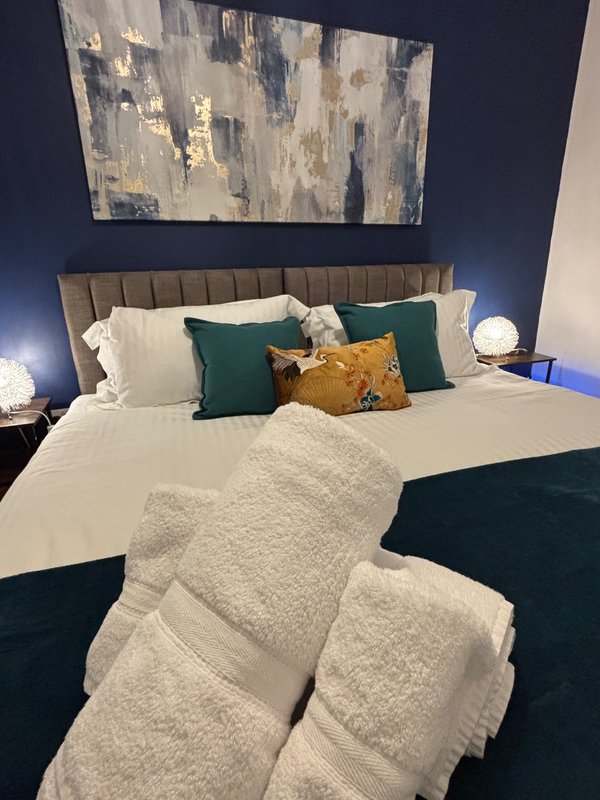 Modern bedroom with king bed, teal headboard, layered bedding and decorative pillows