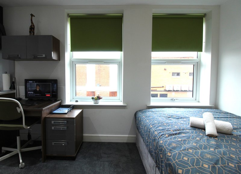 Bedroom with single bed, desk, chair, and two windows with green roller blinds