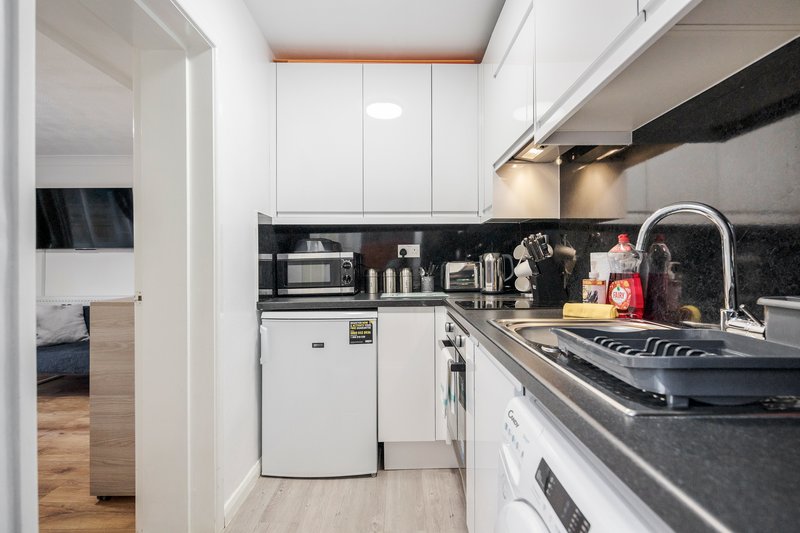 Compact galley kitchen with white cabinetry, black countertop, white appliances and sink