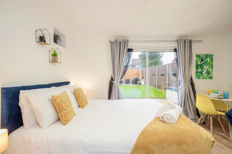 Modern bedroom with double bed, yellow and white pillows, blue headboard, garden view through patio doors