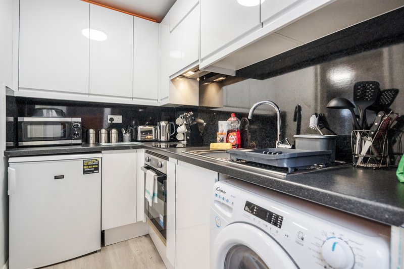 Modern kitchen with white cabinetry, black countertop, built-in appliances and washing machine