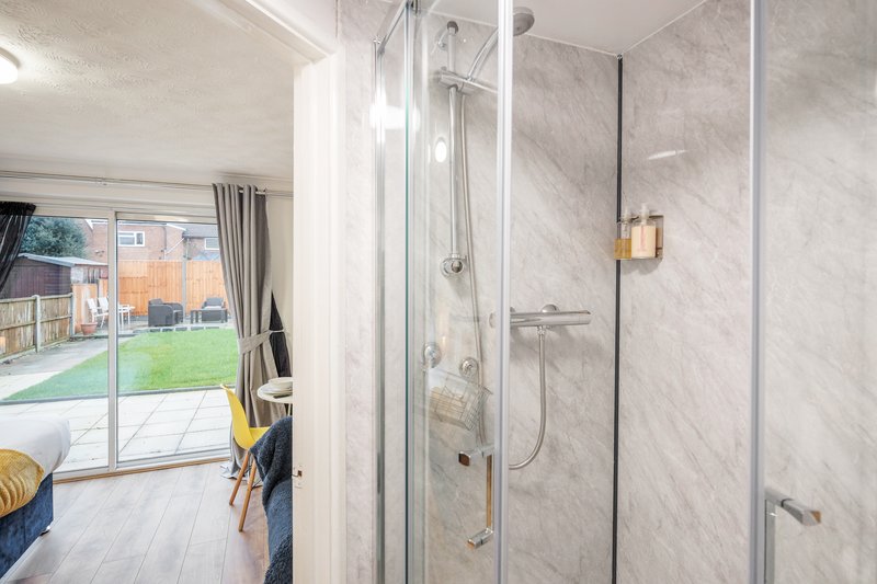 Modern bathroom with marble-tiled walk-in shower, glass enclosure, and view to garden beyond