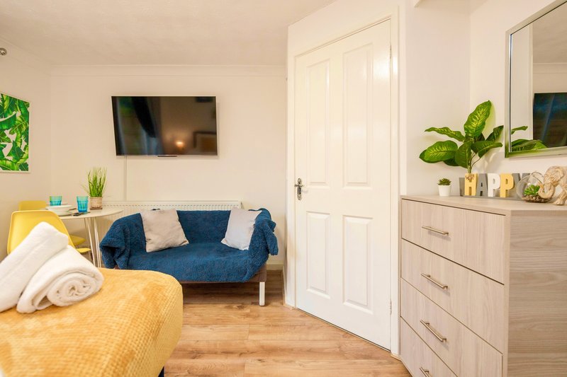 Bright bedroom with double bed, blue sofa, wooden dresser and potted plants
