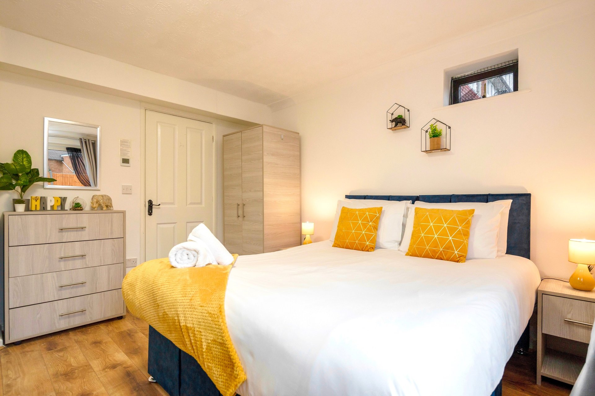 Modern bedroom with double bed, yellow accents, wooden floor and built-in wardrobe