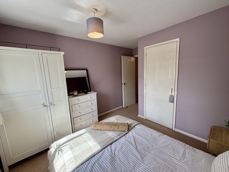 Purple bedroom with double bed, white wardrobe, chest of drawers and pendant light