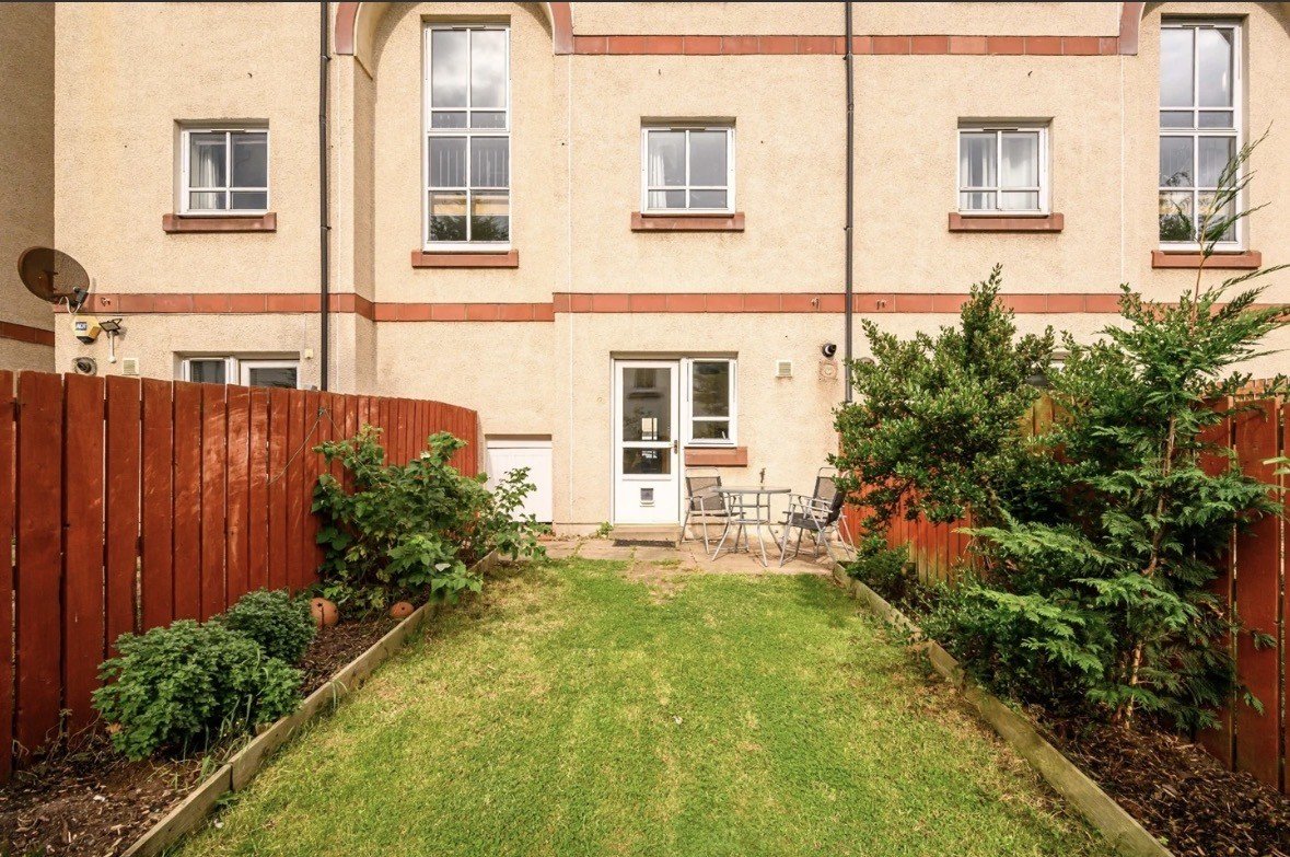 Rear garden with lawn, red wooden fences and terraced house backdrop