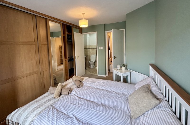 Bedroom with double bed, wooden wardrobe, green walls and ensuite bathroom view