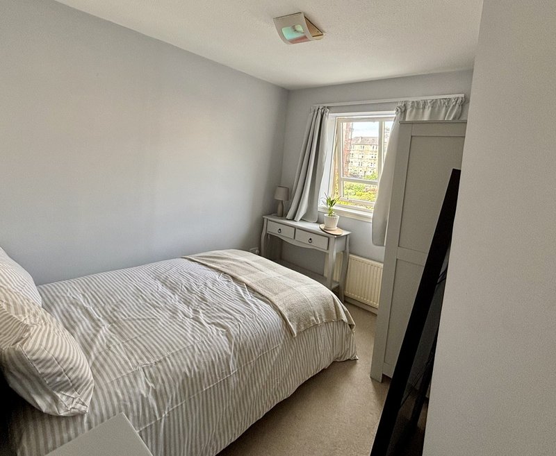 Bright bedroom with striped bedding, window view, desk, and neutral décor
