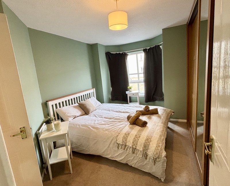 Bedroom with double bed, green walls, white bedside table, pendant light and window