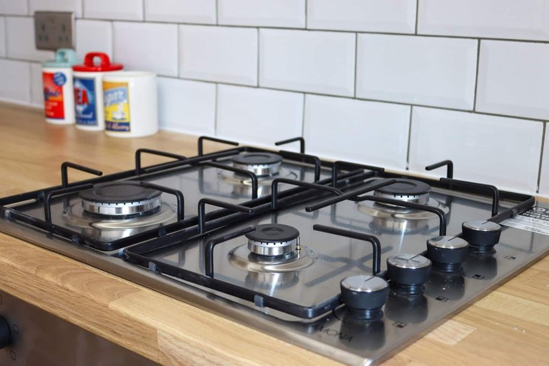 Gas cooktop with four burners on wooden counter, white subway tile backsplash, kitchen items on shelf