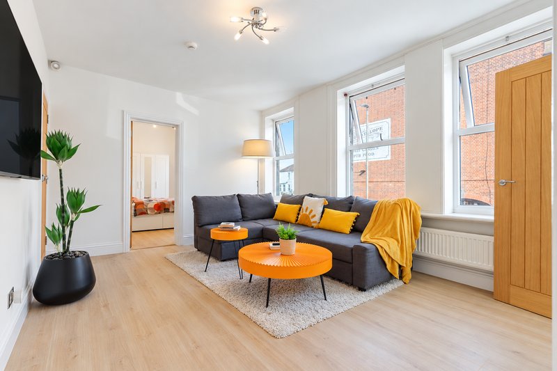Bright modern living room with grey sofa, orange coffee table, wooden flooring and large windows