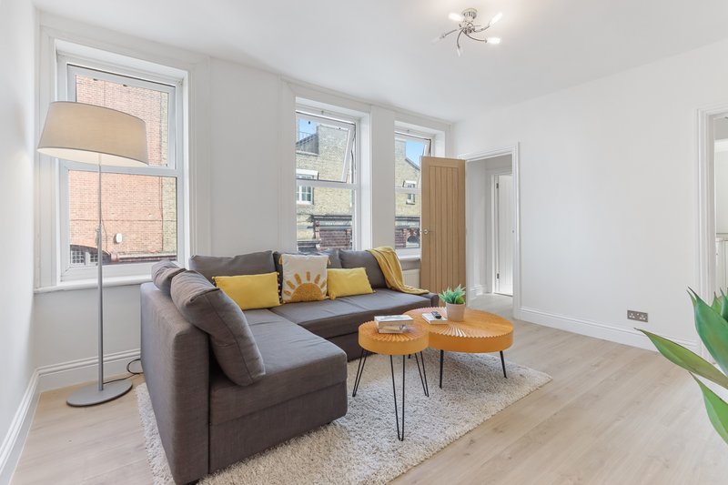 Bright modern living room with gray sofa, wooden coffee tables, yellow cushions and potted plant