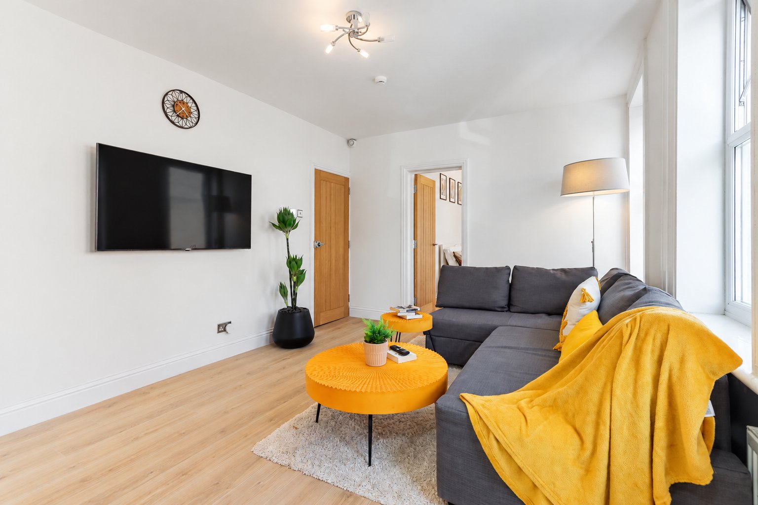 Modern living room with grey sofa, yellow throw blanket, orange coffee table and wall-mounted TV