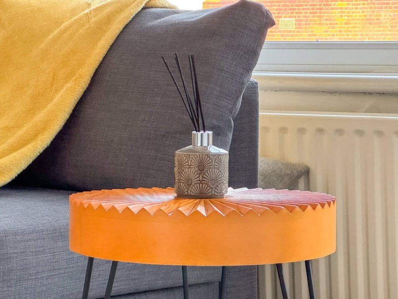 Living room with gray sofa, orange side table, reed diffuser and yellow throw blanket