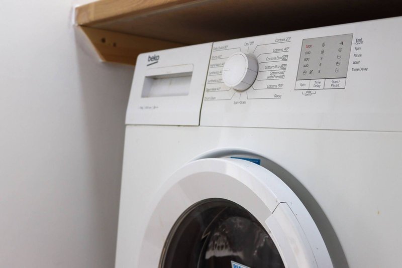 White washing machine with control panel under wooden shelf