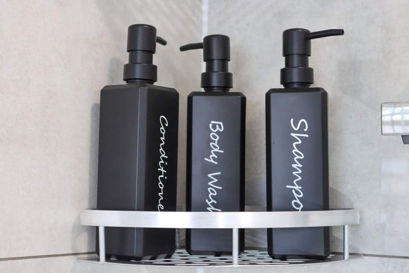 Three black pump bottles with white labels on a bathroom shelf