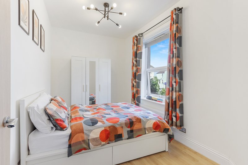 Bright bedroom with single bed, orange patterned bedding, white wardrobe and window with view