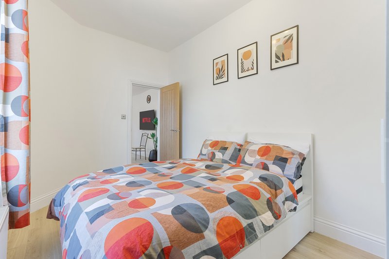 Bedroom with double bed, colorful geometric bedding, wooden wardrobe and framed wall art