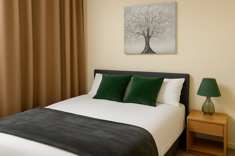 Modern bedroom with double bed, green and white pillows, dark throw, wooden bedside table and lamp