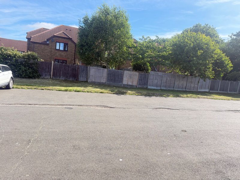 Brick house exterior with driveway, fence, and mature trees under blue sky