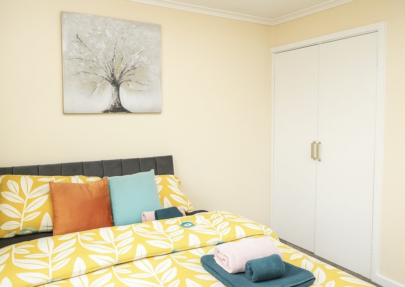 Bright bedroom with yellow patterned bedding, colorful pillows, black headboard and white wardrobe