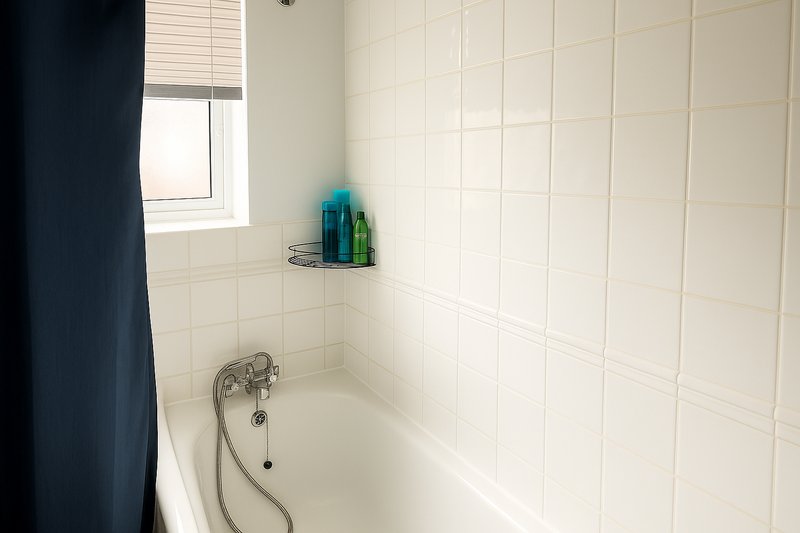 Clean white bathroom with bathtub, shower head, small window and toiletries shelf
