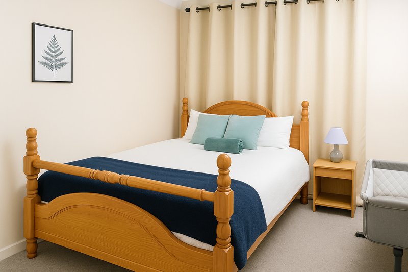 Bedroom with wooden four-poster bed, white pillows, navy bedspread, cream curtains and framed fern artwork