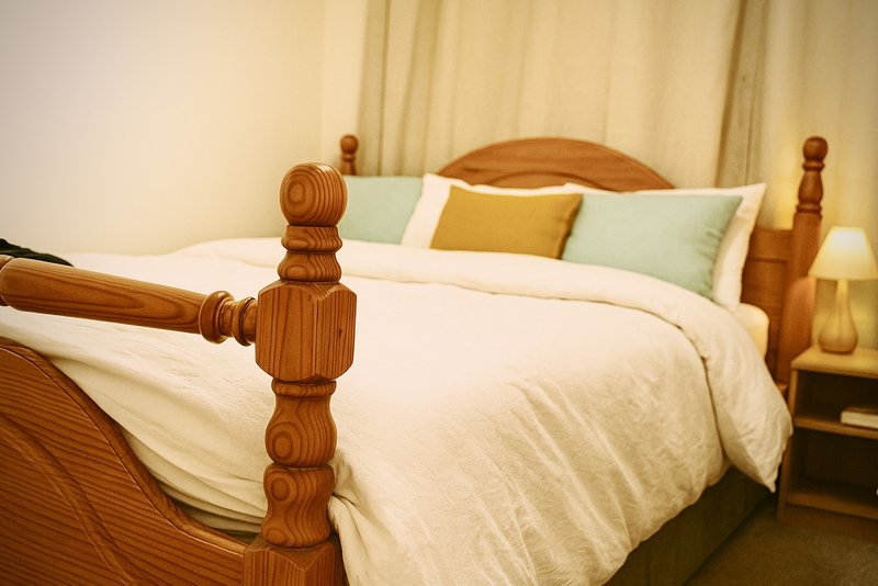 Bedroom with wooden bed frame, white bedding, yellow and green cushions, bedside lamp