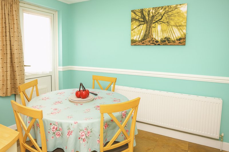 Dining area with turquoise walls, round table with floral tablecloth, yellow chairs and artwork