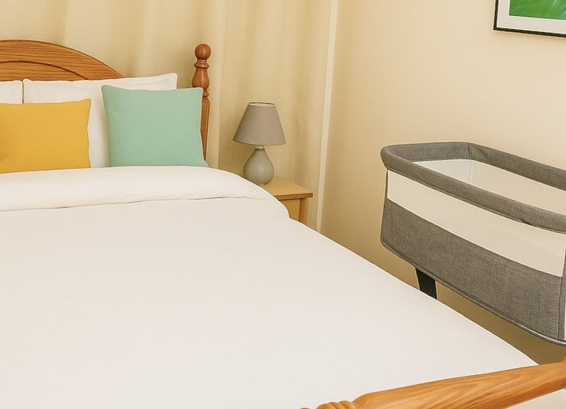 Bedroom with wooden bed frame, white bedding, yellow and green decorative pillows, and crib