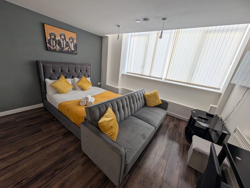 Modern bedroom with grey upholstered bed, yellow cushions, dark wood flooring and large windows