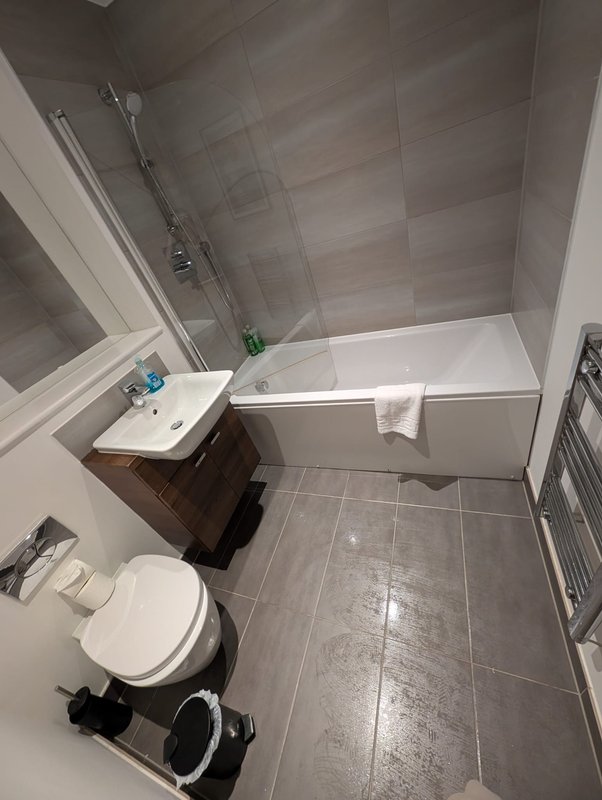 Modern bathroom with gray tile walls, white toilet, sink, and bathtub with shower