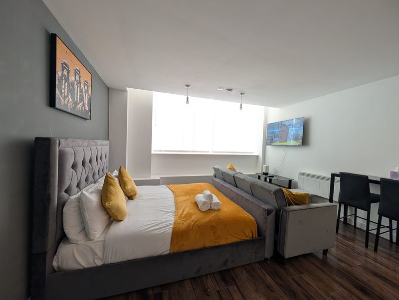 Modern bedroom with double bed, gold cushions, white bedding, and sitting area by window