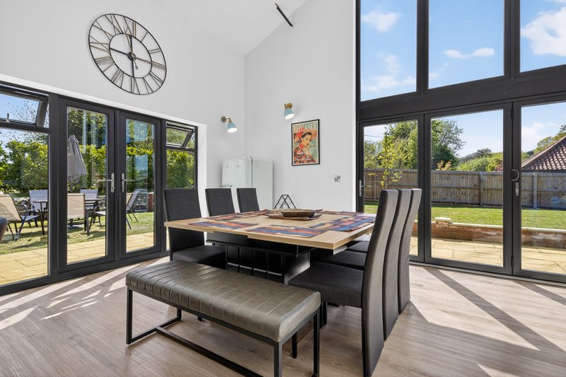 Modern dining room with wooden table, black chairs, bench seating, large windows overlooking garden