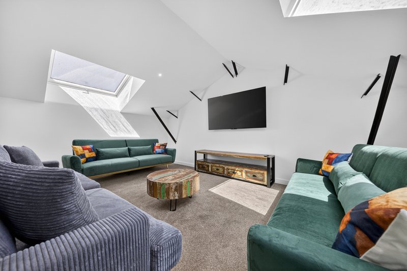 Modern attic living room with green and blue sofas, wall-mounted TV, fireplace, skylight and cushions
