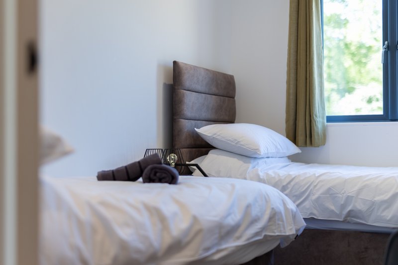 Bedroom with two single beds, white pillows, upholstered headboard, and window with blue frame