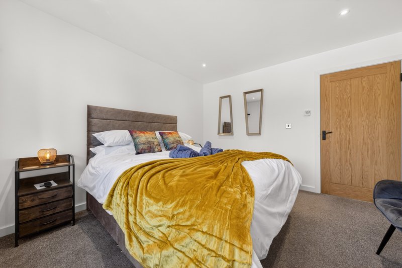 Modern bedroom with double bed, yellow throw, wooden bedside table and grey carpet